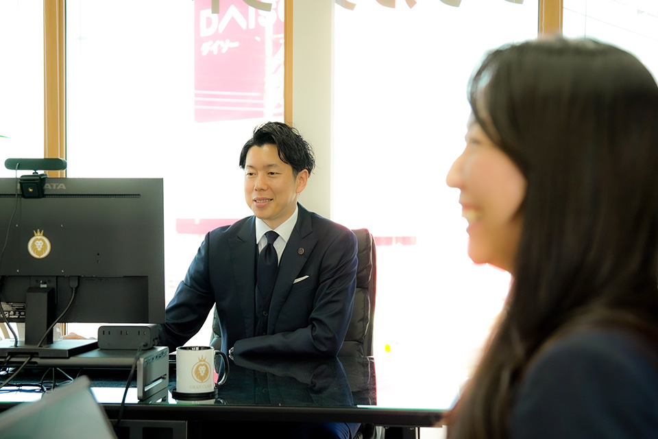 窓際で椅子に座るスーツ姿の男性が真剣な眼差しで前方を見つめている。